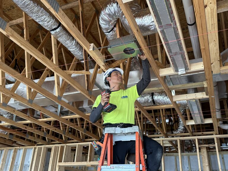 Construction worker on ladder installing ceiling ductwork