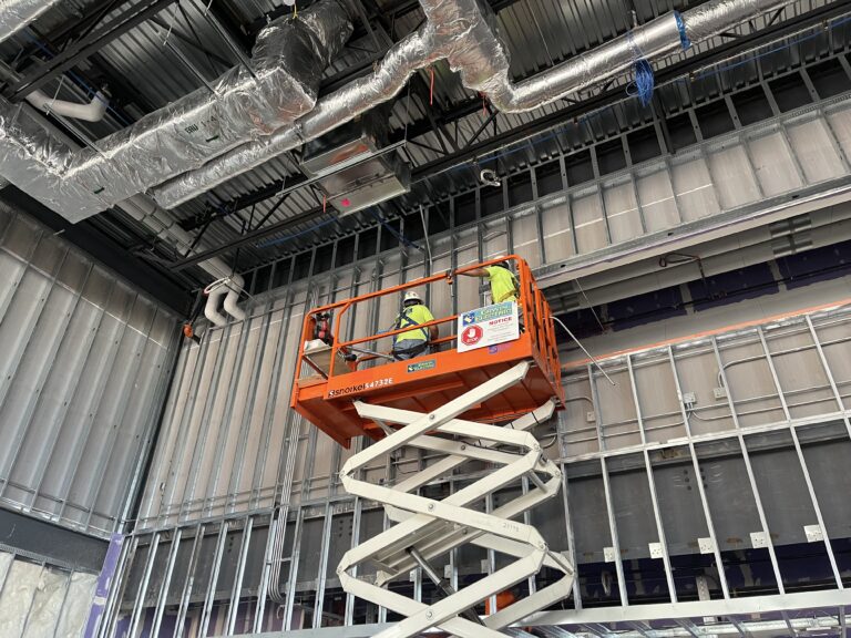 Construction workers on scissor lift installing ceiling ducts