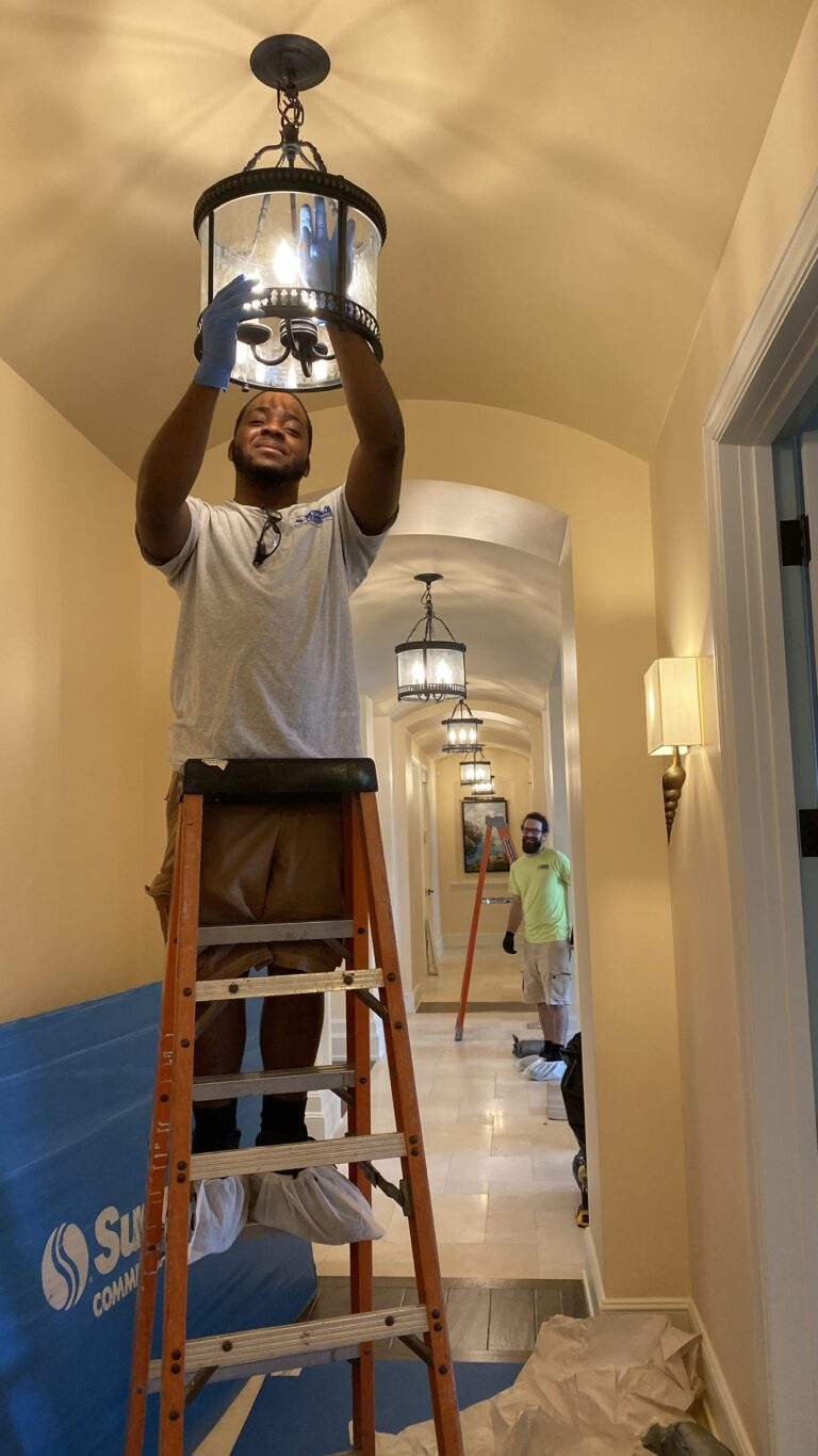 Worker on ladder installing hallway chandelier